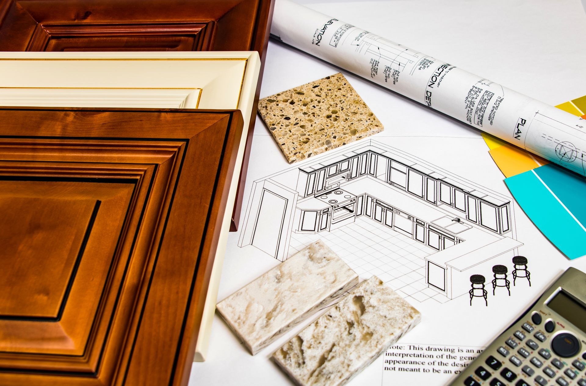 Kitchen design plans with cabinet samples, stone swatches, and calculator on table.