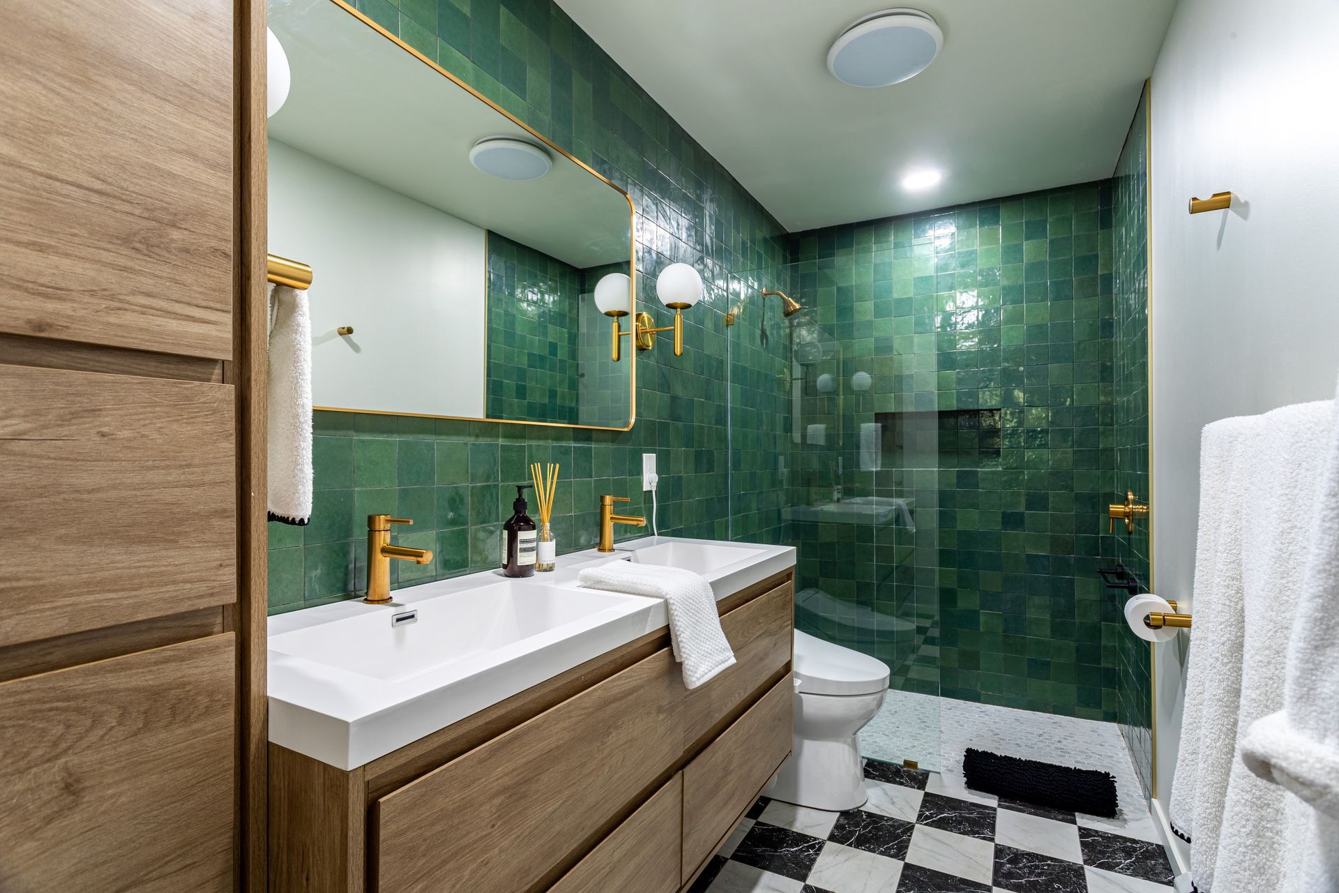Modern bathroom with green tiled shower, white vanity, and black-and-white checkered floor.