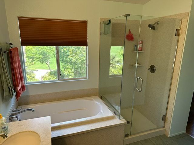 Bathroom with soaking tub, glass shower, and window with brown blind overlooking greenery
