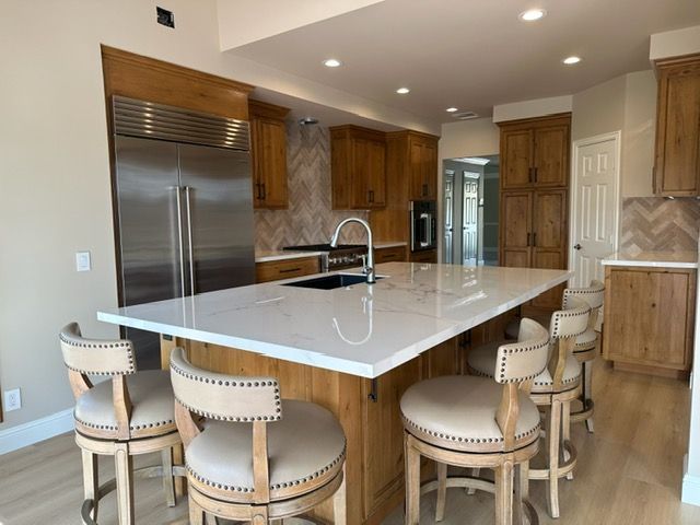 Modern kitchen with large marble island, four stools, stainless steel appliances, and wood cabinets