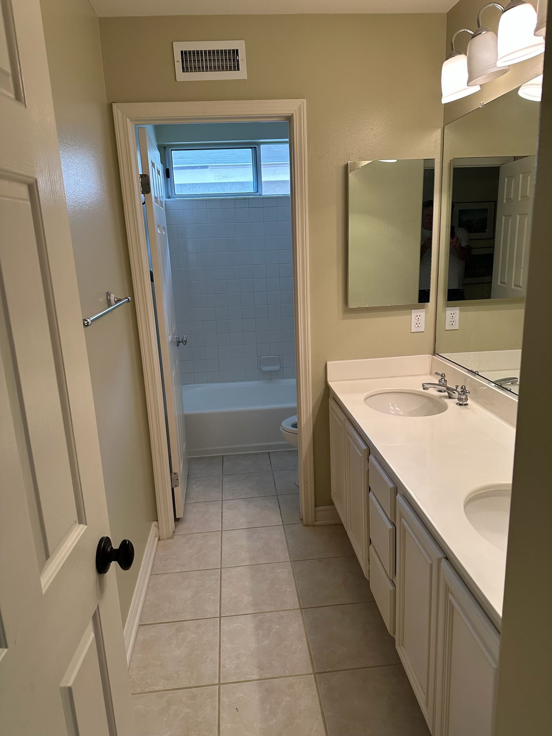Bathroom with double vanity and mirrors, tiled floor, and a shower visible through the doorway.