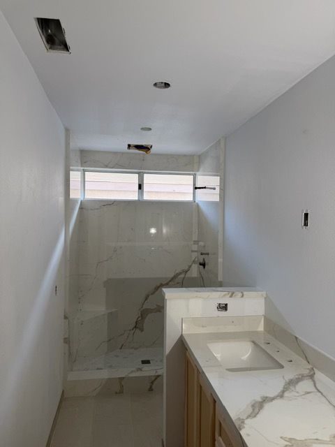 Narrow unfinished bathroom with white tile shower, vanity sink, and ceiling light cutouts