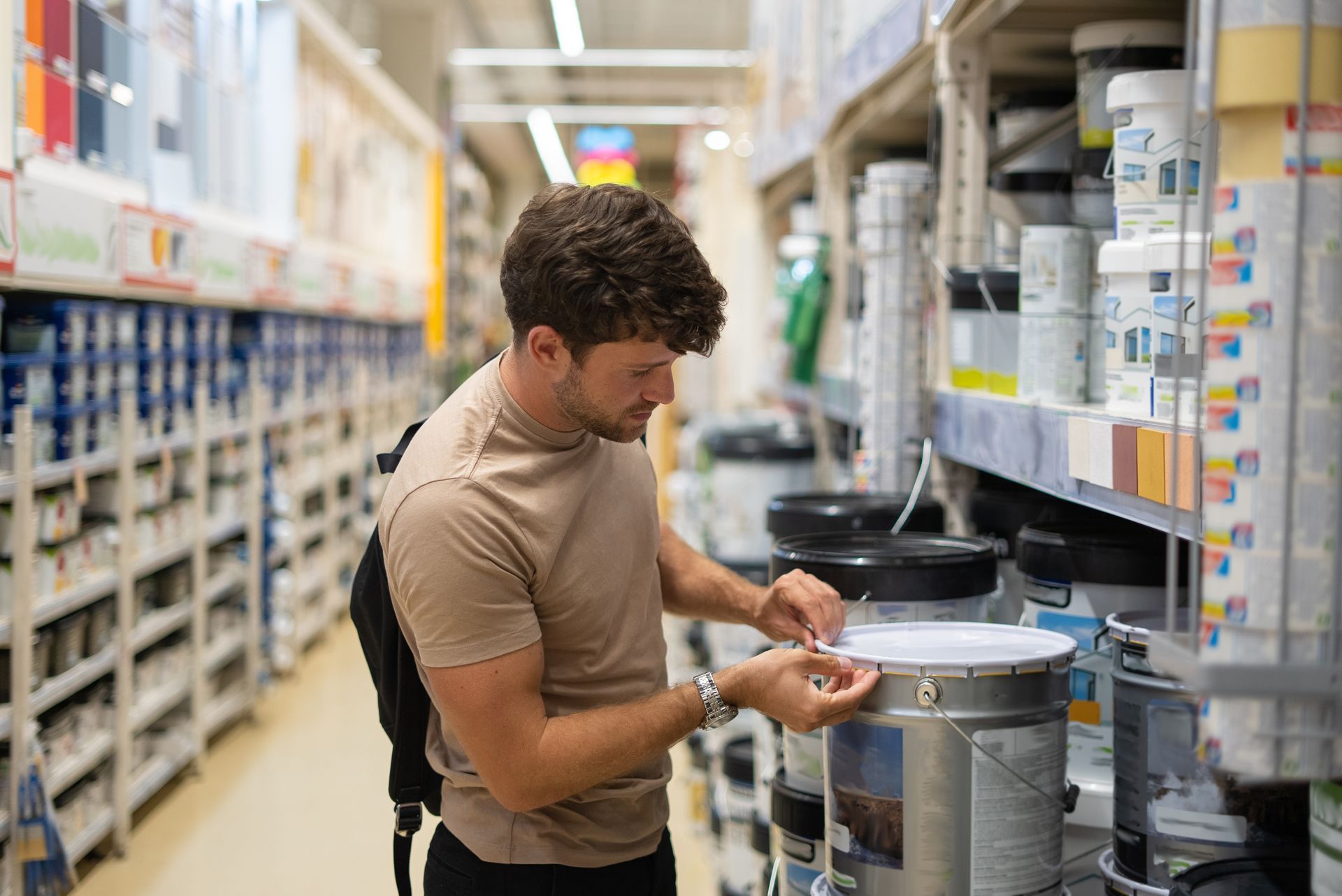 Person examines a paint can label in a store aisle lined with paint supplies. Person examines a paint can label in a store aisle lined with paint supplies.