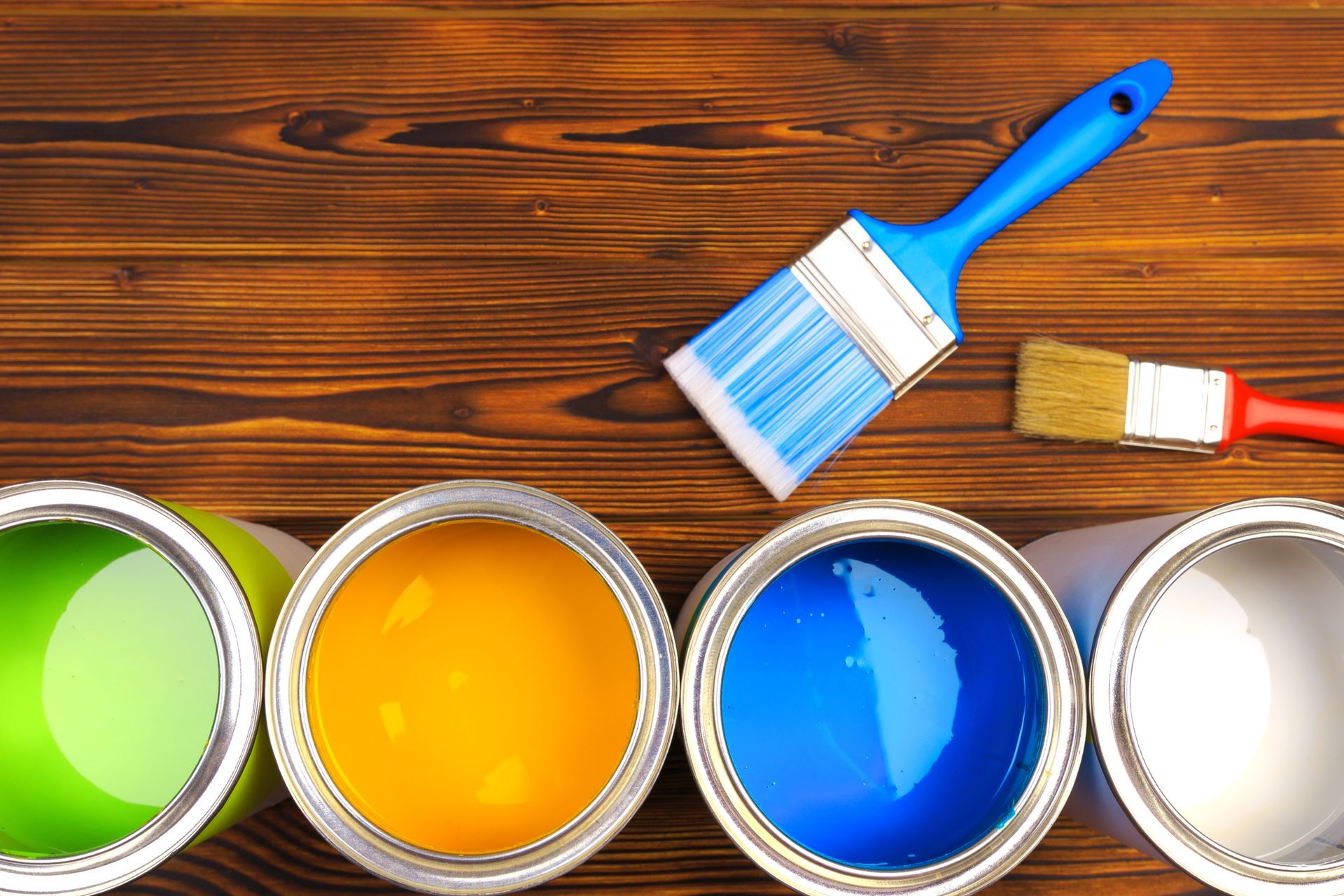 Four open paint cans with brushes on a dark wood surface. Four open paint cans with brushes on a dark wood surface.