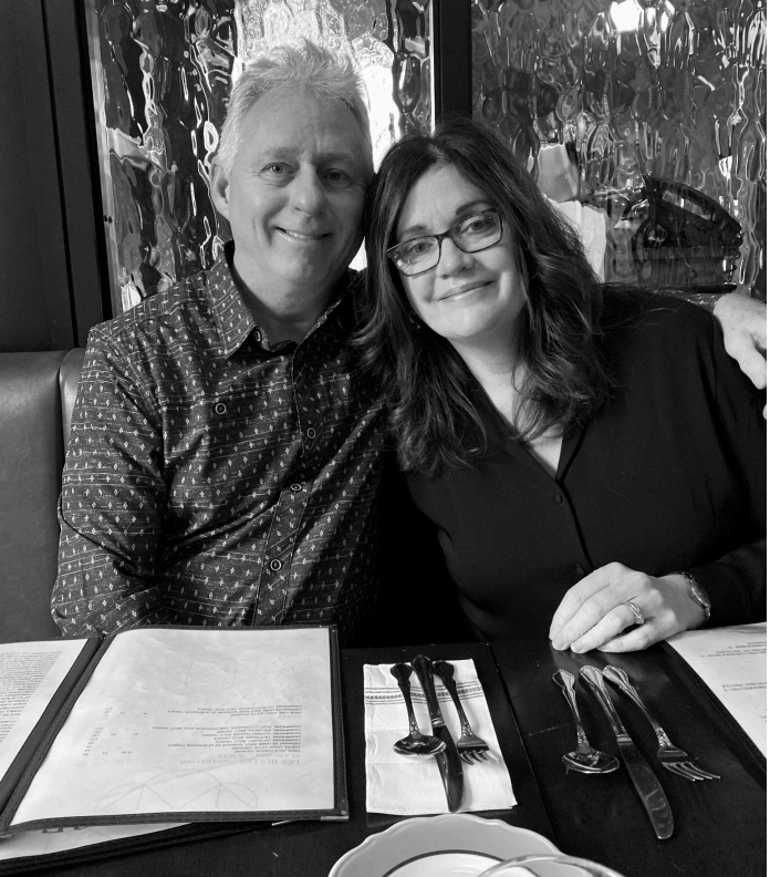 A couple smiling while sitting at a restaurant table with menus and silverware.