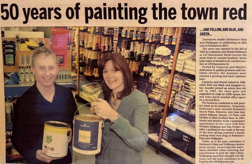 A man and woman smile while holding paint cans in a hardware store, beneath the headline 