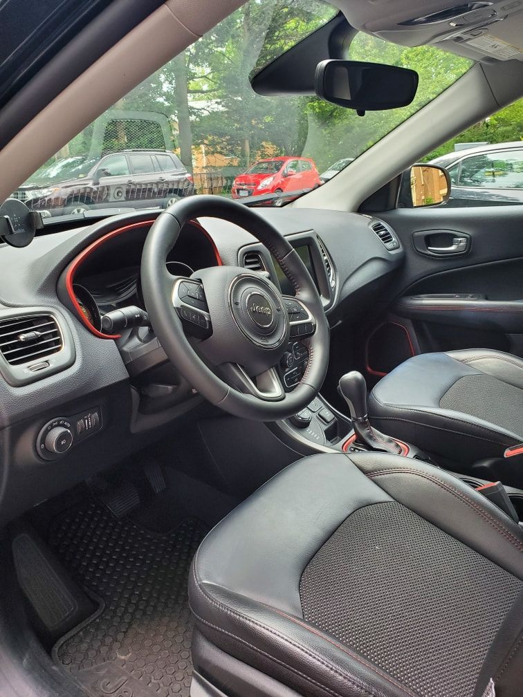 Interior view of a Jeep Compass with black leather seats, steering wheel, and dashboard. Red accents are visible.