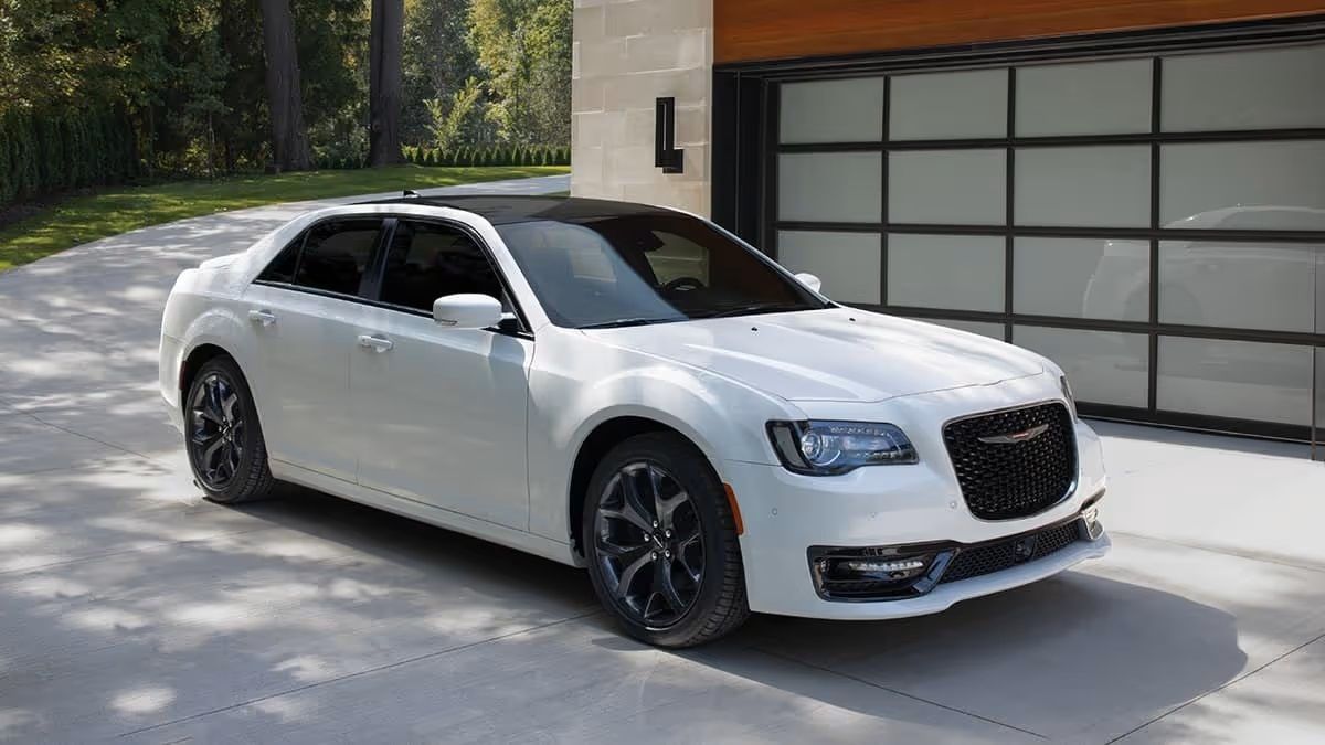 White Chrysler 300 sedan with black roof parked on a paved driveway in front of a modern home.