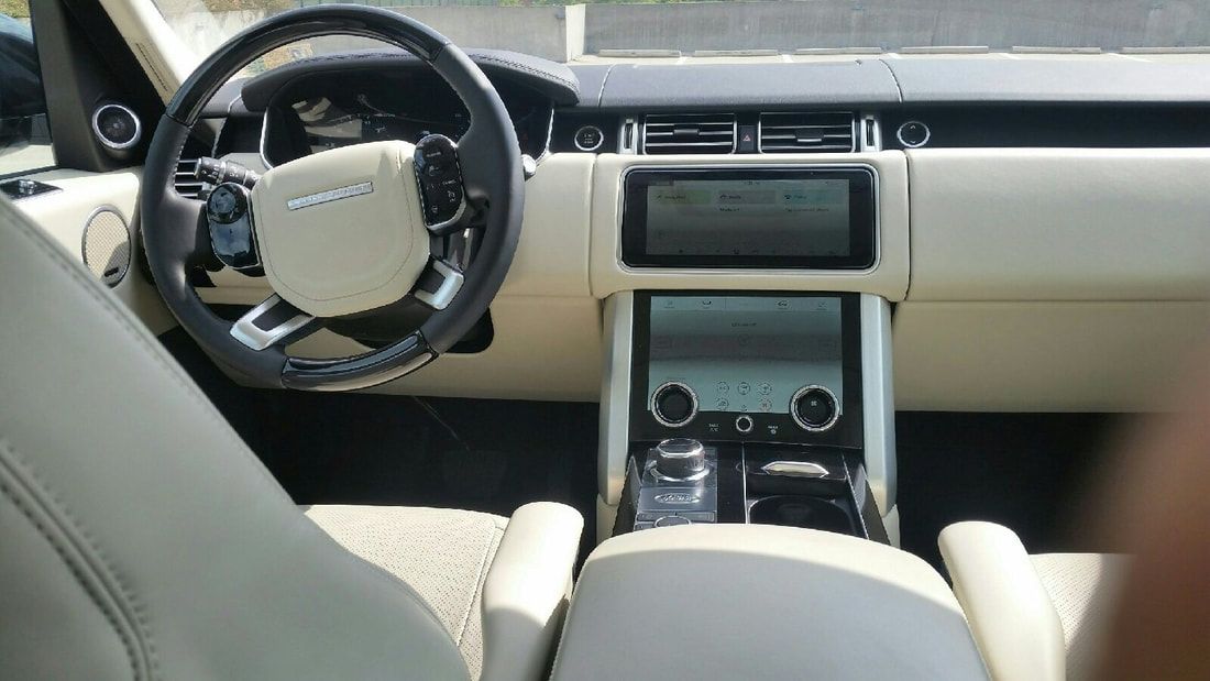 Cream-colored interior of a Land Rover Range Rover. Dashboard with two screens, steering wheel, and front seats.