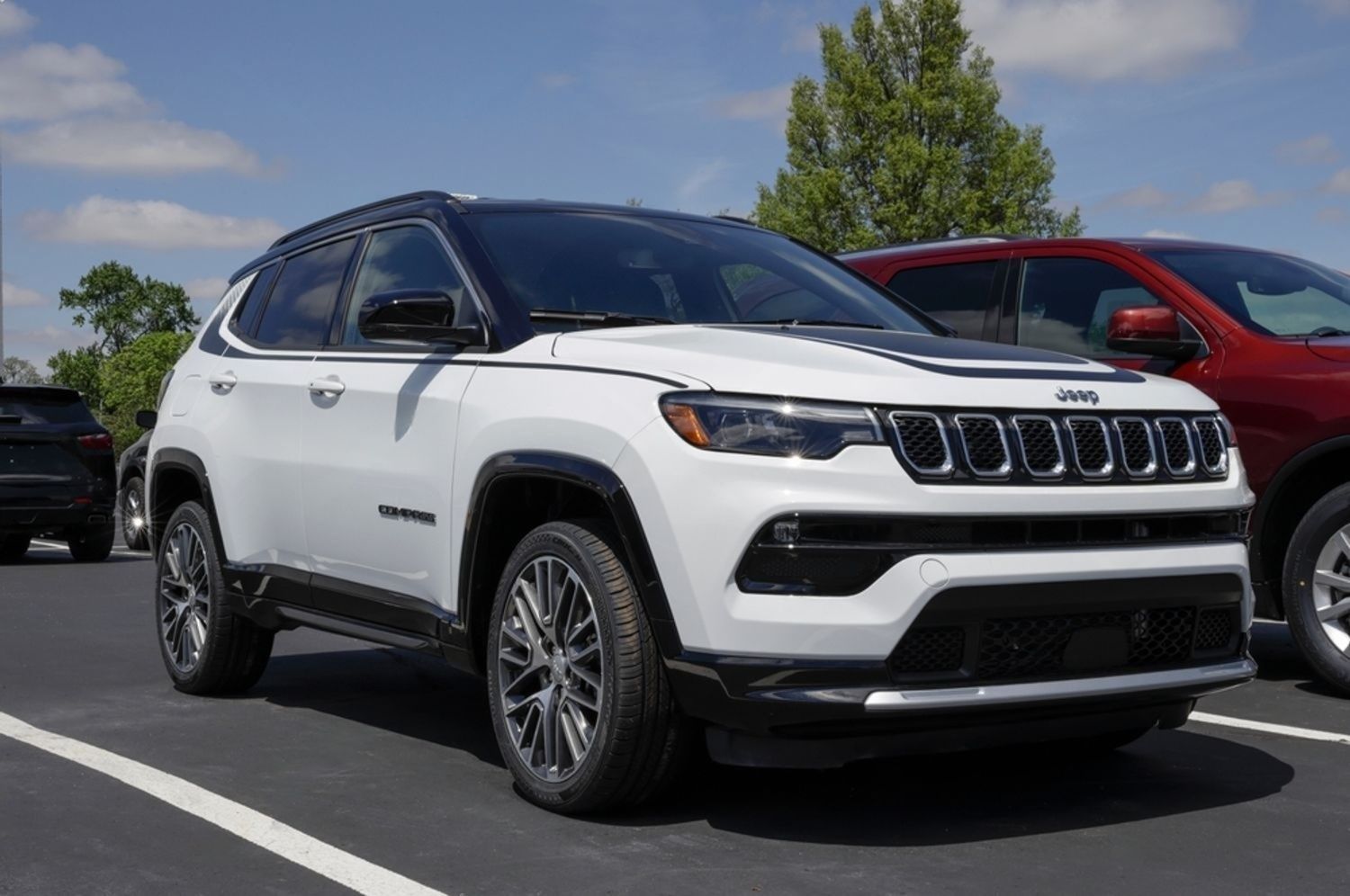 White Jeep Compass parked in a lot, black roof and hood accents, sunny day.