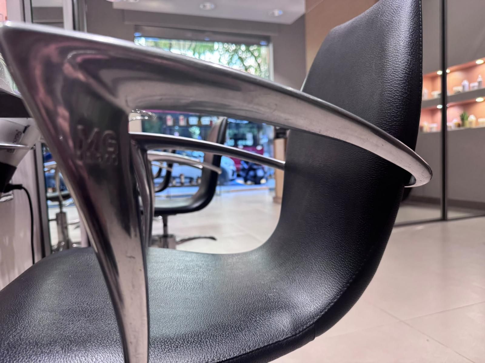 Sedia moderna in rete nera in uno showroom con vetrine e braccioli cromati riflettenti.