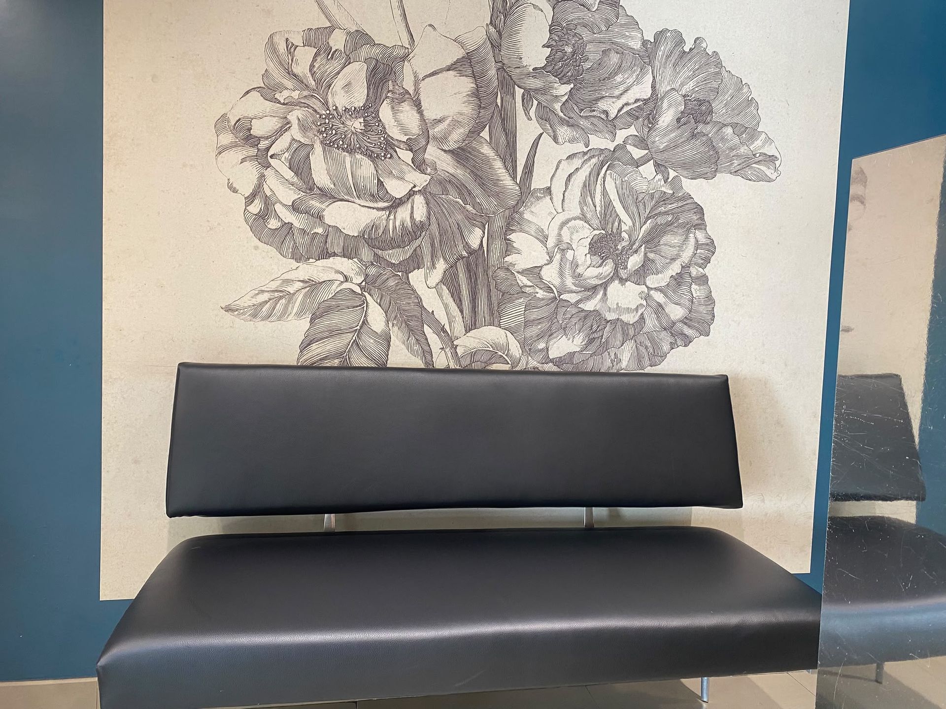 Panchina nera sotto un murale floreale in una moderna sala d'attesa.