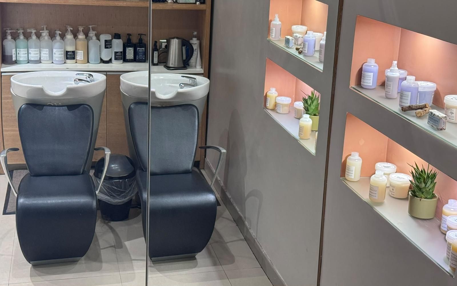 Postazioni per lo shampoo in un salone di bellezza, con sedie nere, lavandini a specchio e scaffali pieni di prodotti per capelli e candele.