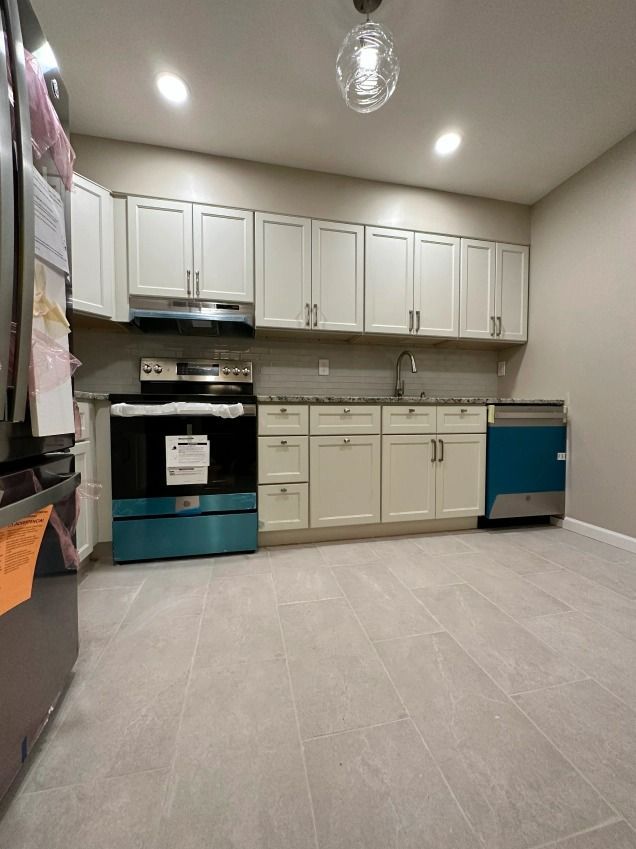 A kitchen with white cabinets , a stove , a refrigerator , and a dishwasher.
