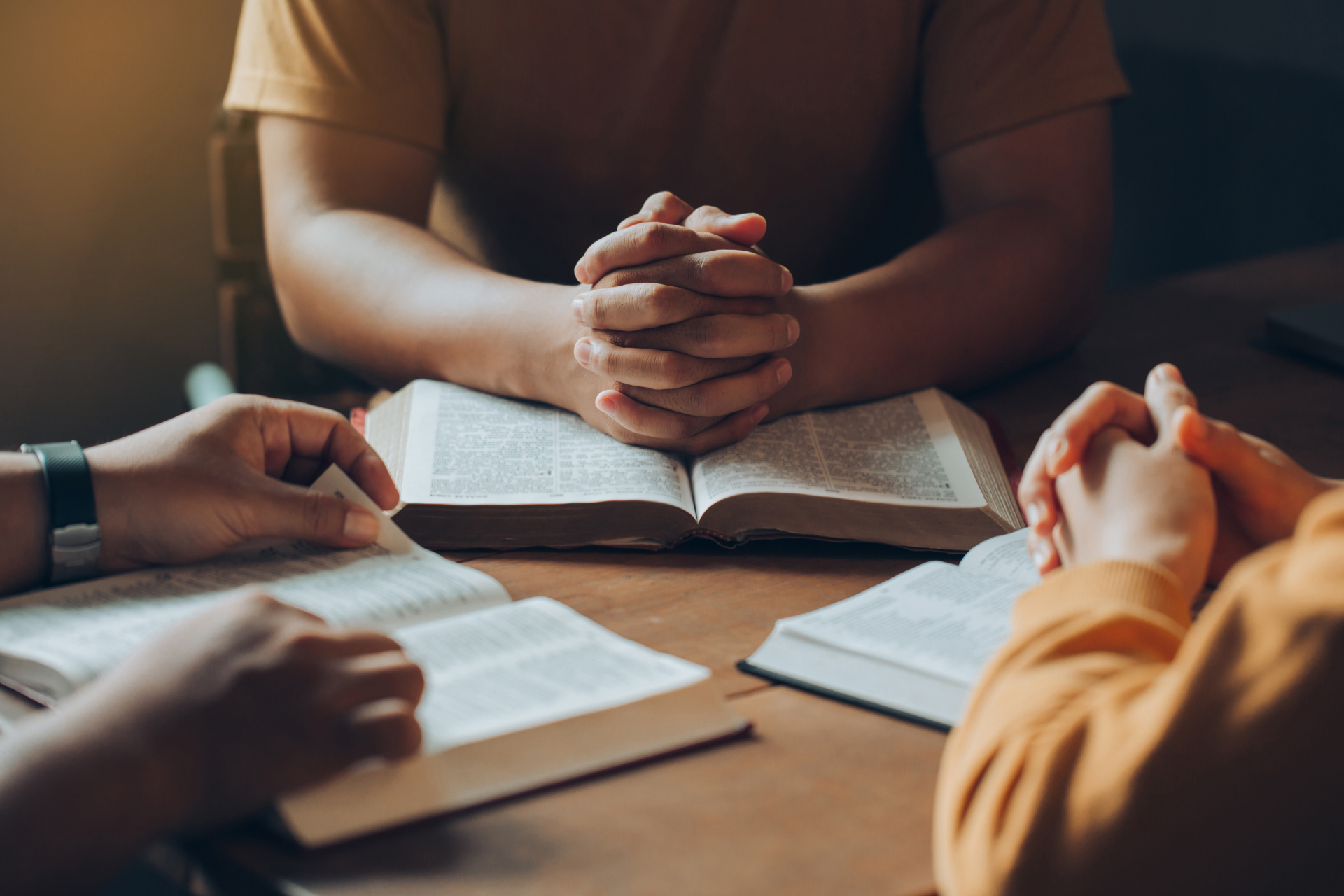 People gathered around an open book, hands clasped in a warm-lit discussion.