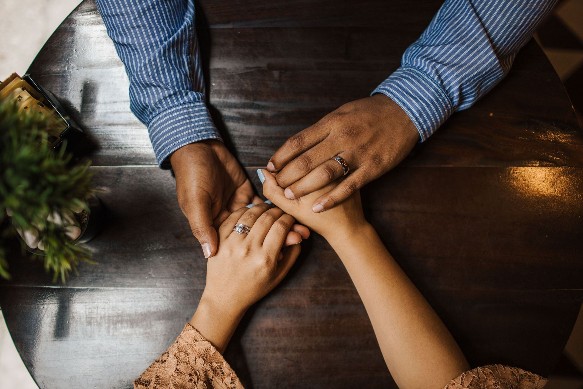 Three people stack hands over a wooden table in a warm, overhead view.