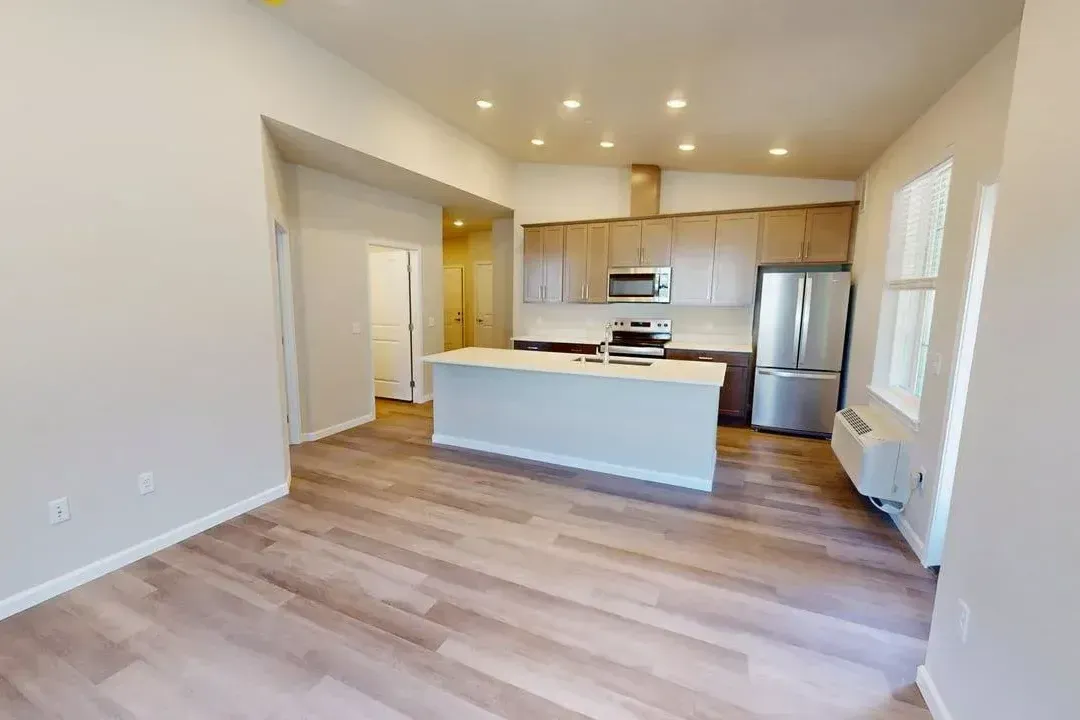 A living room with hardwood floors and a kitchen with stainless steel appliances.