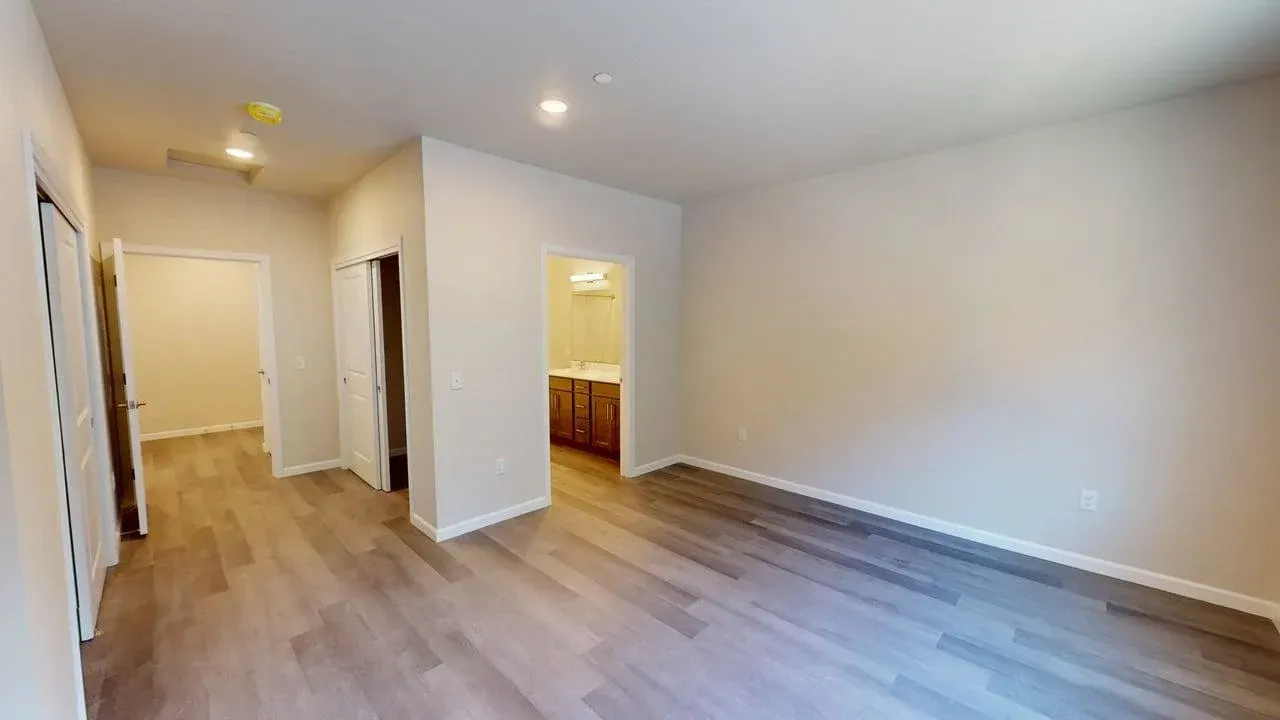 A living room with hardwood floors and a bathroom in the background.