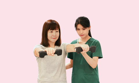 Caregiver assisting woman in workout clothes holding dumbbells against a pink background