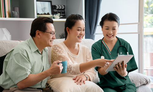 Three people on a couch looking at a tablet with a care manager in green scrubs pointing at the screen