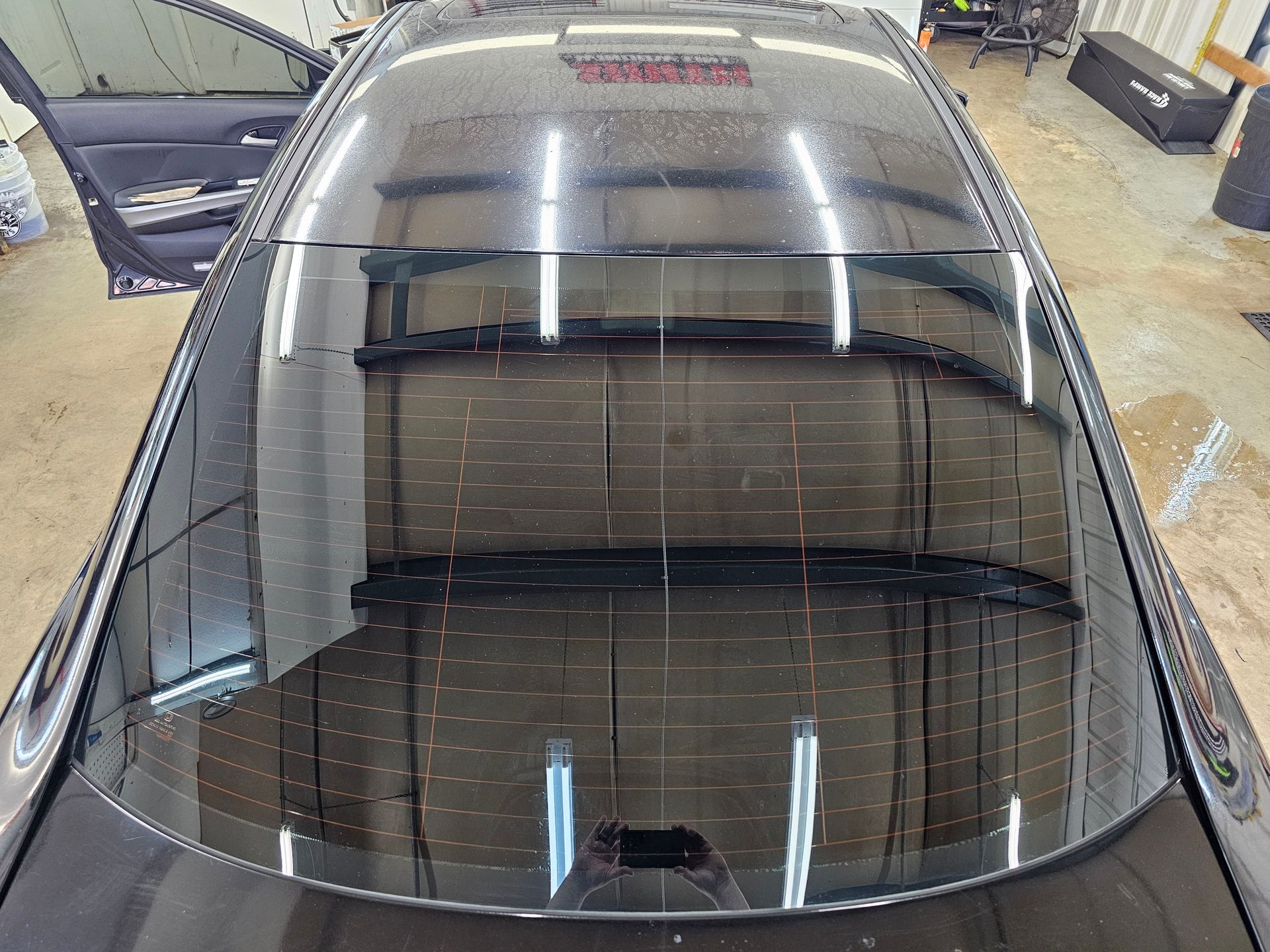 Top-down view of a car's shiny black roof reflecting a room, with a partially open door on the left.