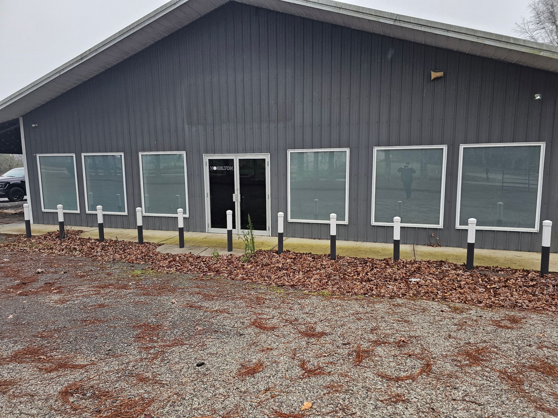 Gray building with multiple windows and a door. Brown leaves and gravel in front.