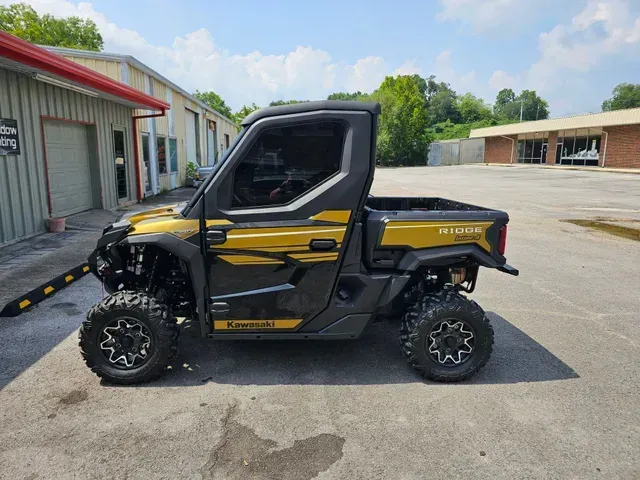 Gold and black Kawasaki Mule side-by-side utility vehicle parked outside.