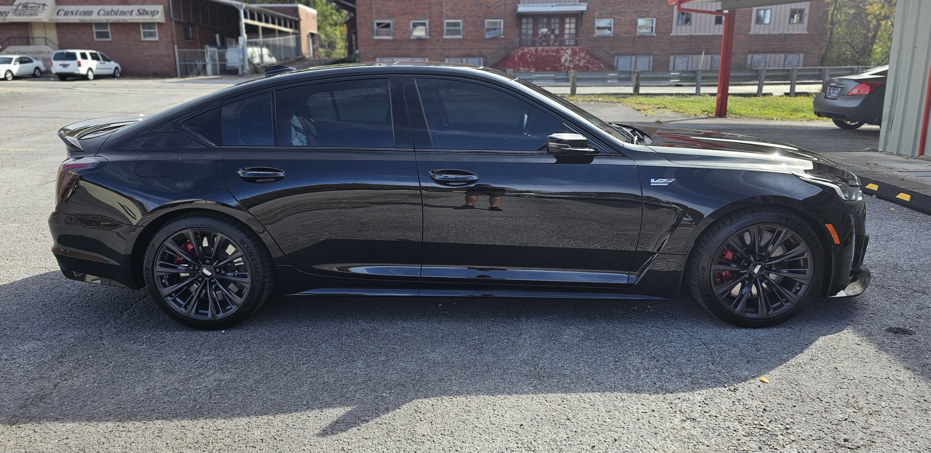 Black Cadillac sedan parked on gravel. Buildings in background.