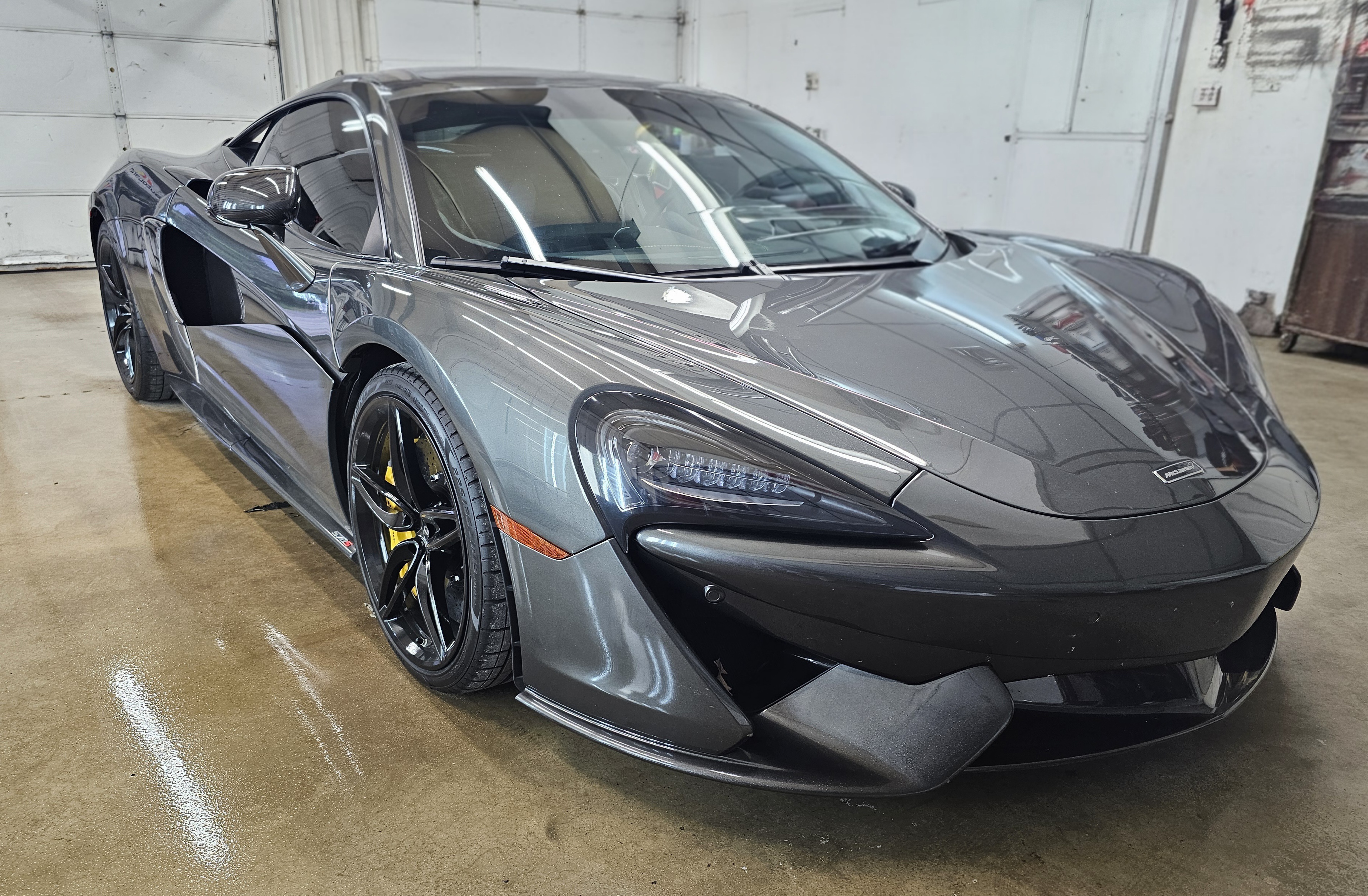 Gray McLaren sports car parked in a car wash, wet with water.
