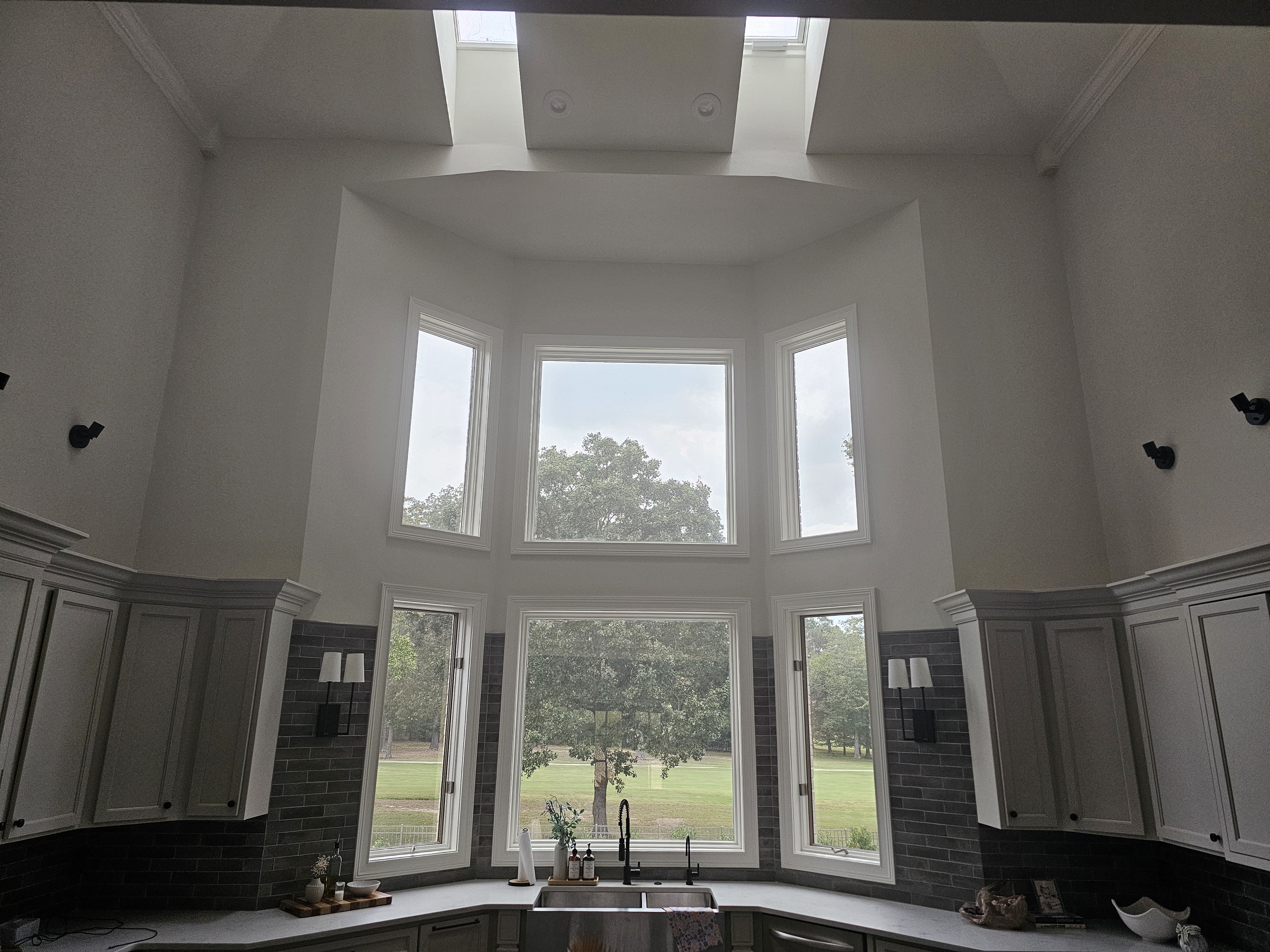 Kitchen with large bay windows overlooking a tree; cabinets below, skylights above.