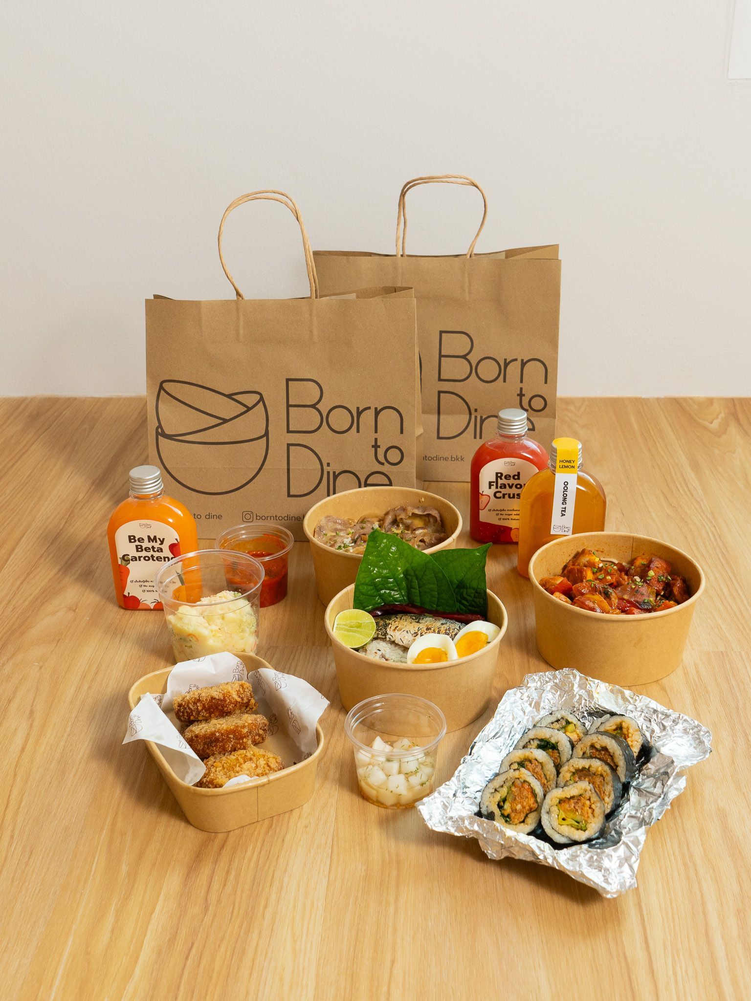 Takeout food spread, including bowls, bottles, rolls, and bags on a wooden table.