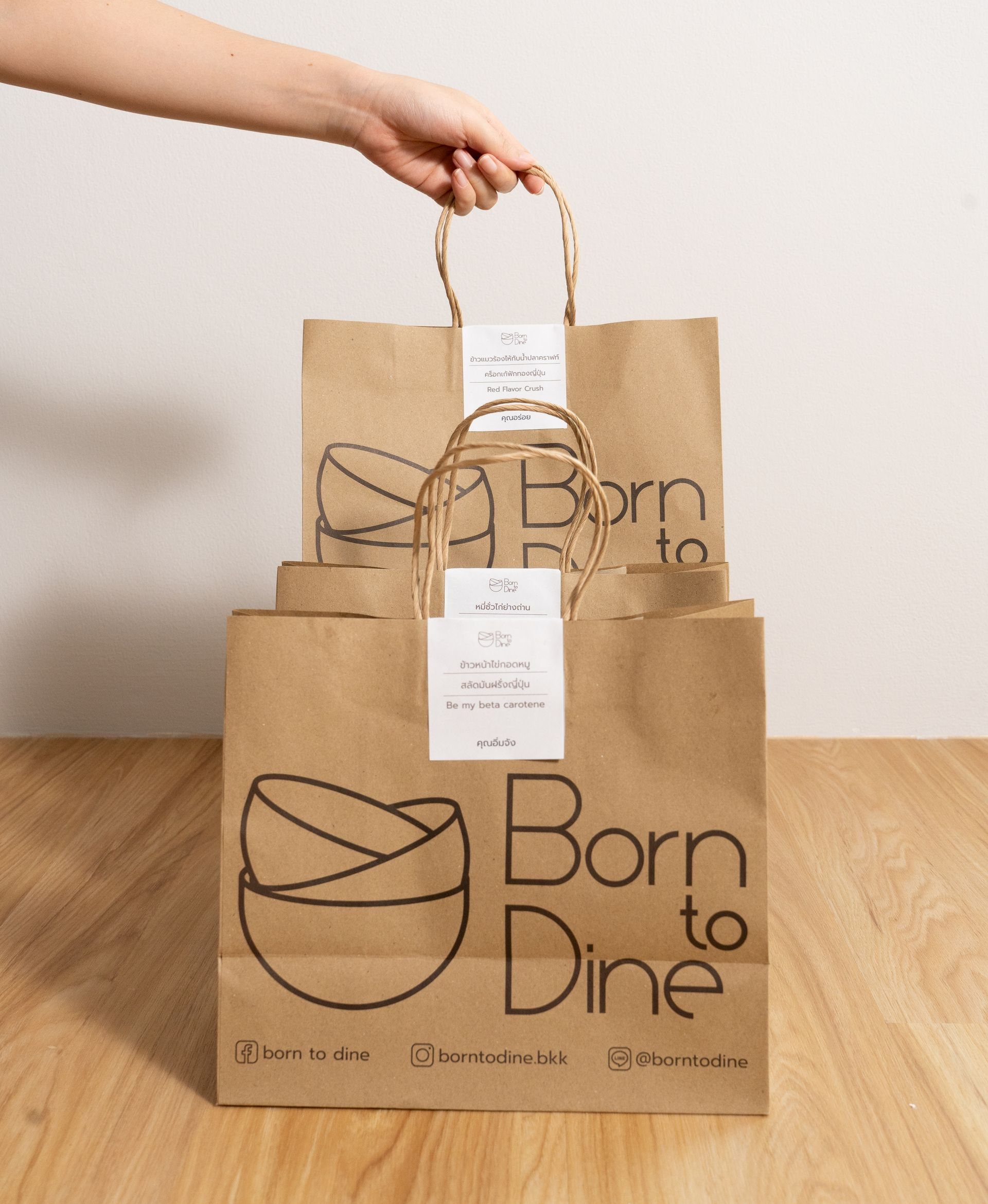 Hand holding three brown paper bags stacked, labeled