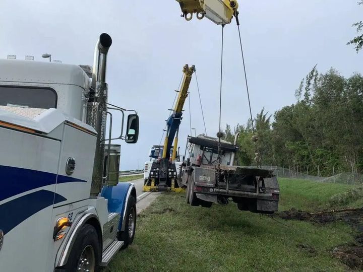 Tow trucks and a crane lifting a vehicle from a roadside ditch on a grassy shoulder