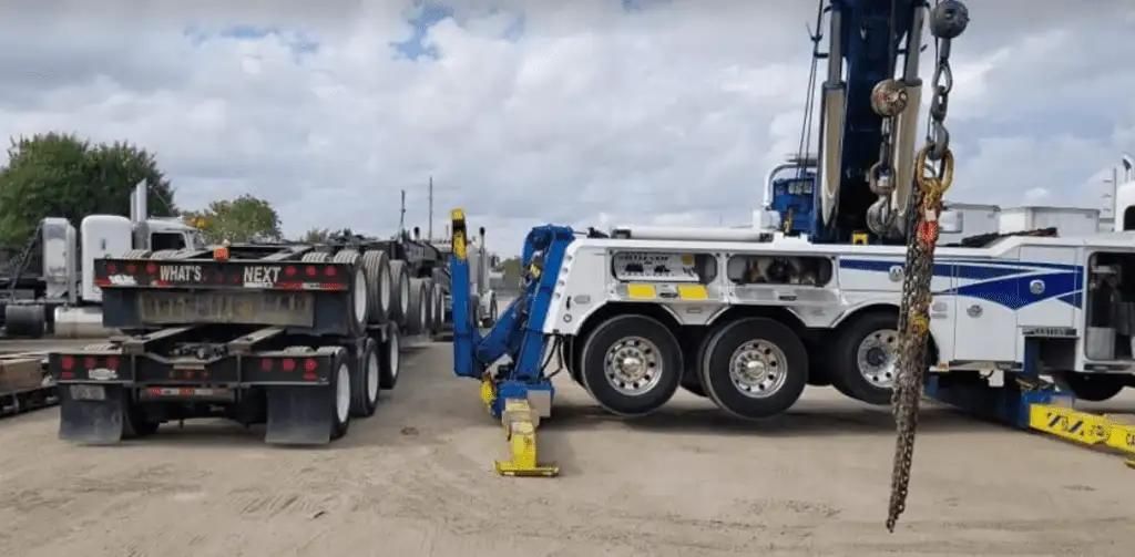 Tow truck lifting a white heavy-duty vehicle with yellow wheel chocks on a roadside lot