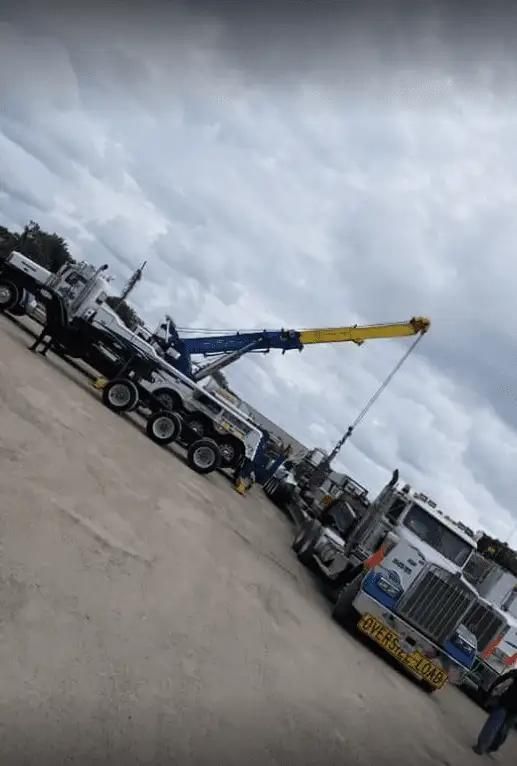 Tow trucks and a crane in a lot under cloudy skies, with a blue-and-yellow boom extended.