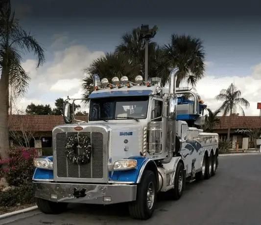 Chrome semi-truck with multiple axles parked on a street near palm trees and buildings
