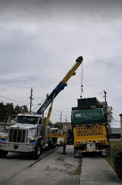 Tow truck lifting a green dump truck on a roadside under a cloudy sky