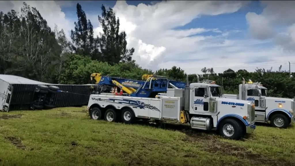 White tow trucks parked on grass near a building, with trees and cloudy sky in the background.