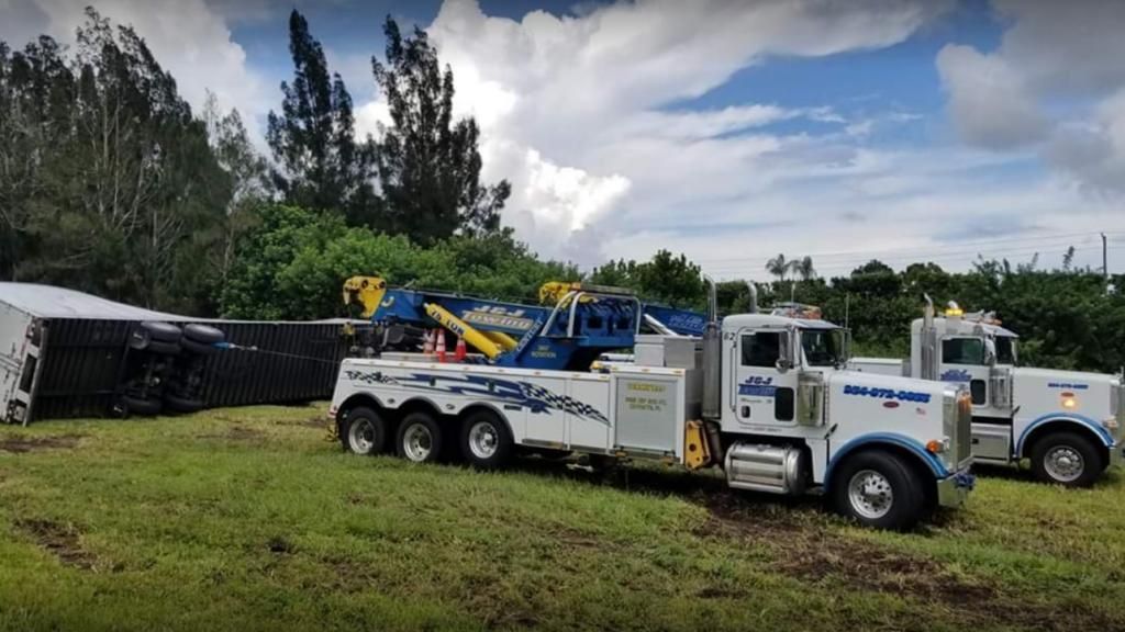 Two white tow trucks parked on grass beside trees under a cloudy sky