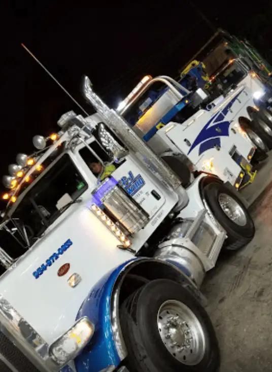 White and blue tow truck with amber lights parked at night on a street
