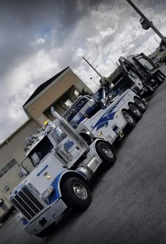 White and blue tow trucks parked in a line on a city street under cloudy skies