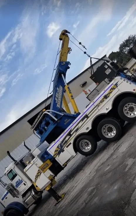 White tow truck with a blue crane arm parked on a roadside under a cloudy sky