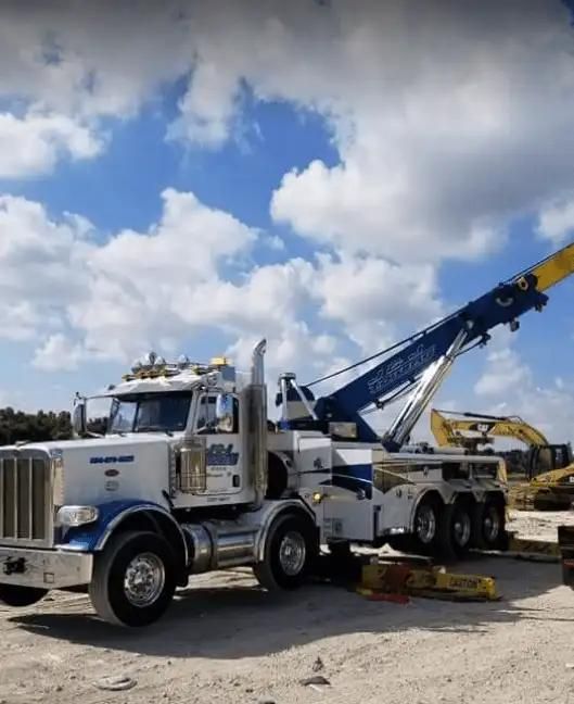 Tow truck lifting a yellow car in a gravel lot under a cloudy blue sky
