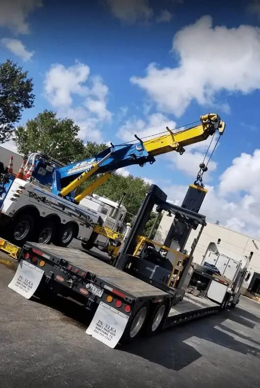 Tow truck flatbed with blue-and-yellow crane parked outdoors under a cloudy sky