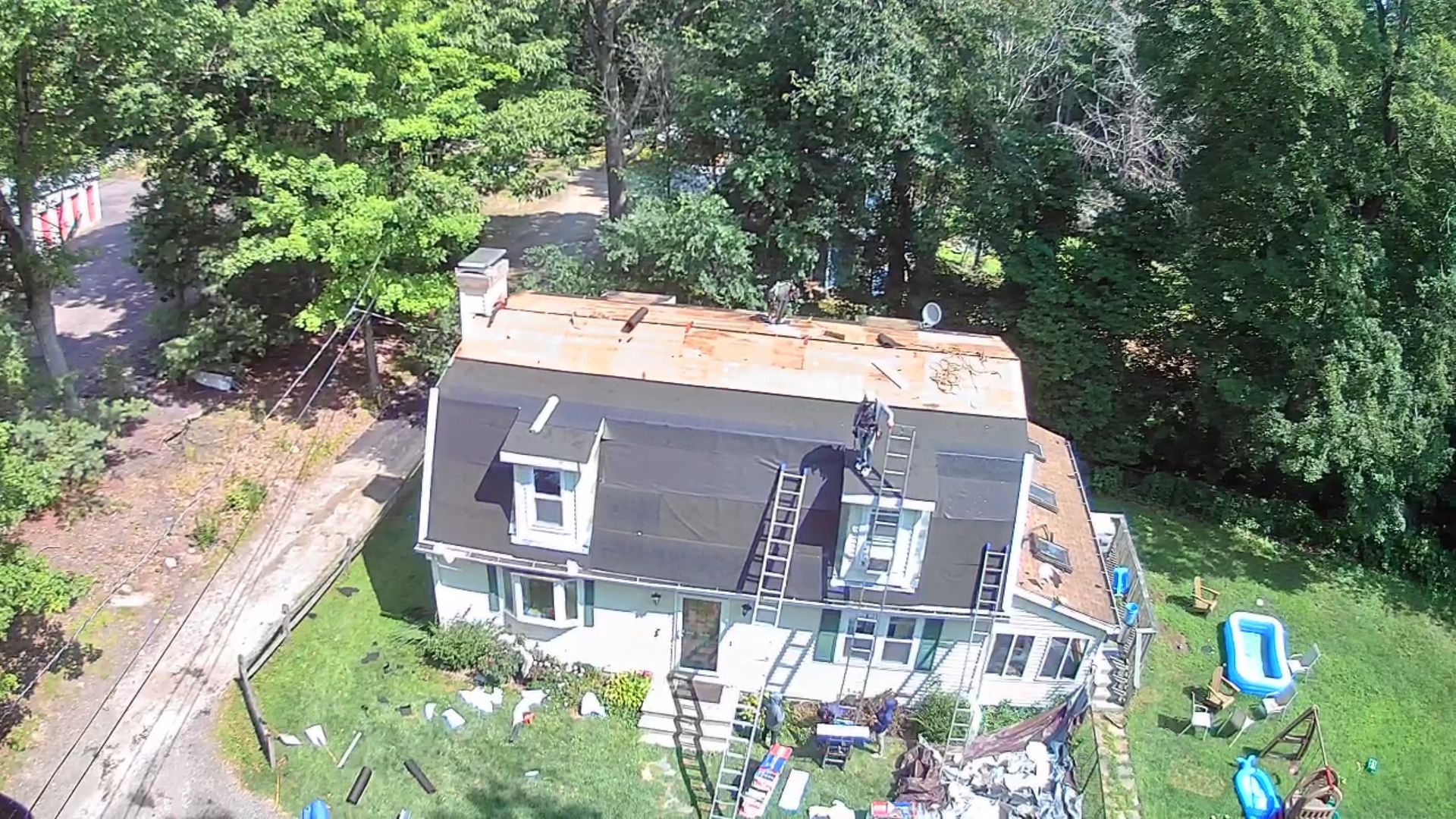 Aerial view of a gray house with a deck and backyard, surrounded by trees and lawn