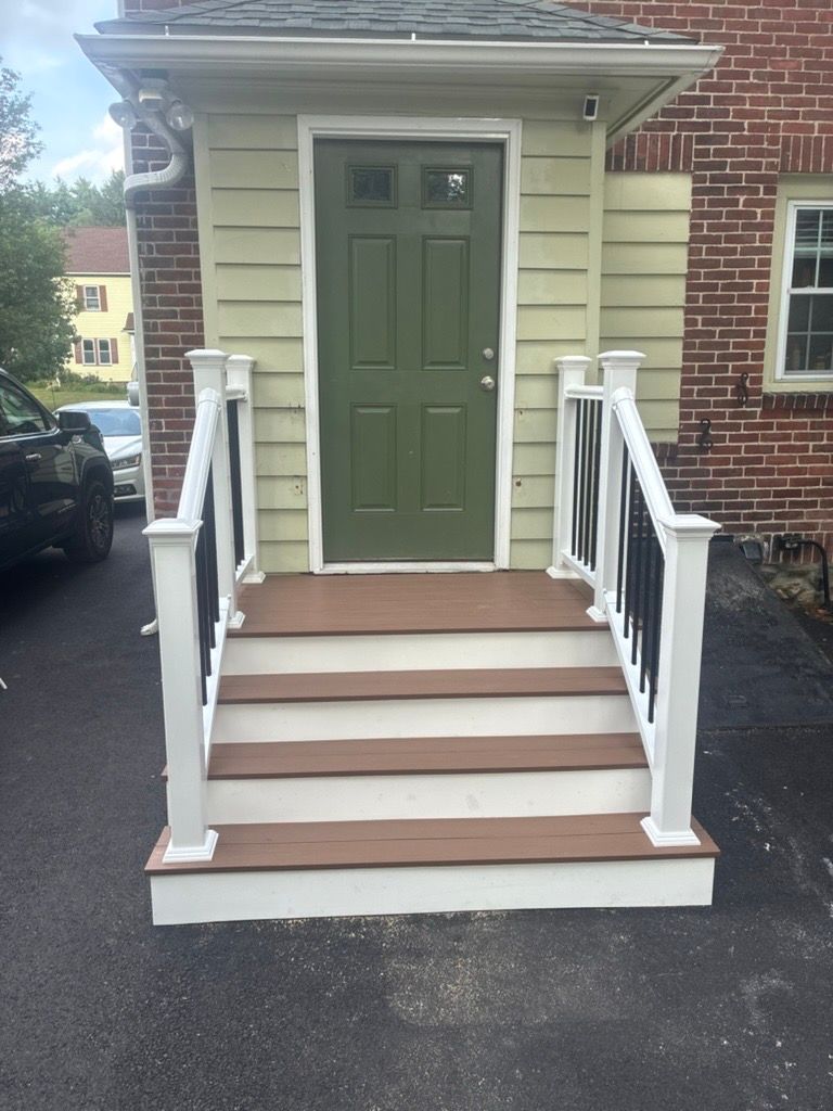 Front steps with white railings leading to a green door on a beige and brick house.