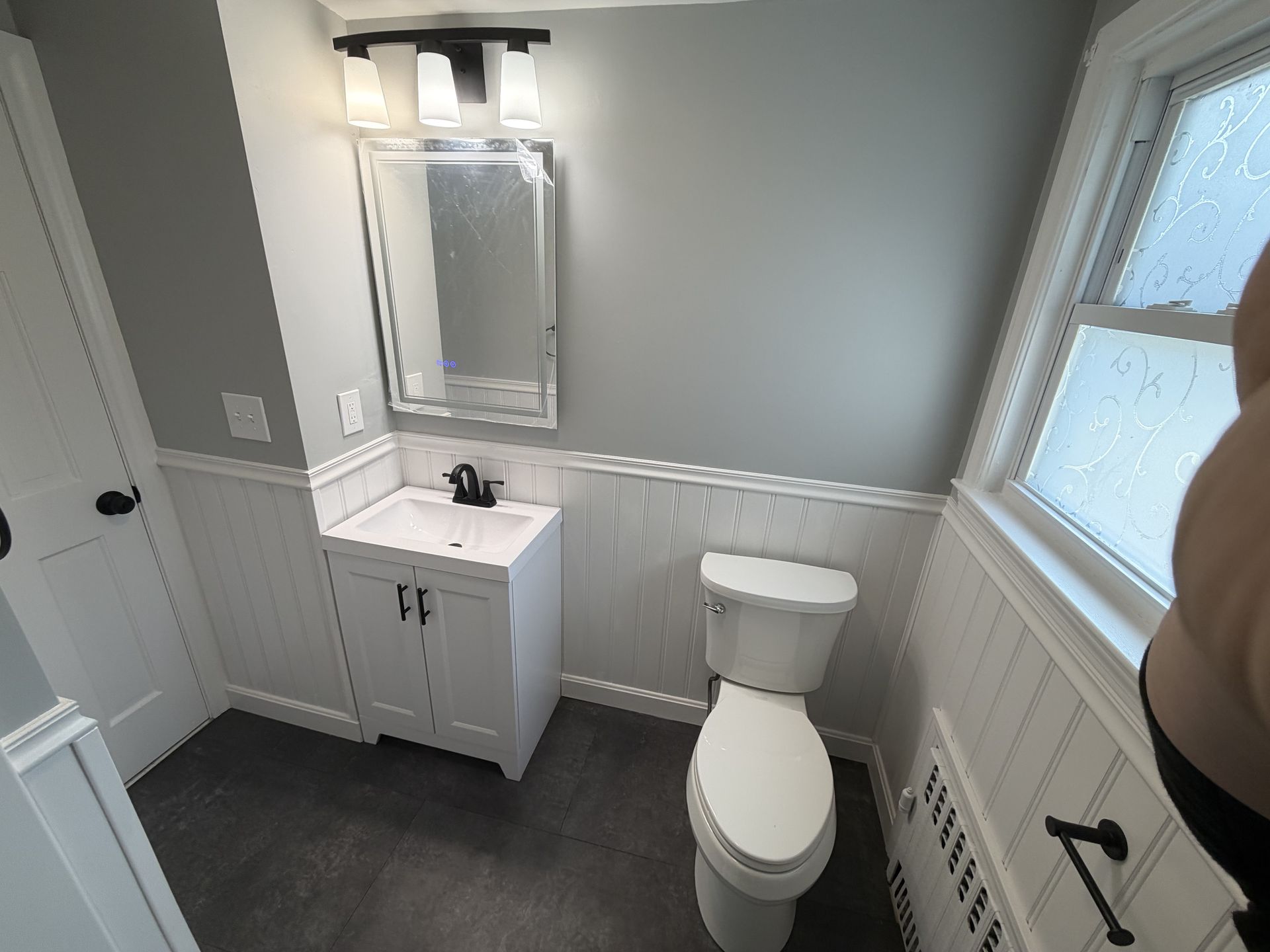 Bright beige bathroom with glass shower, white sink, window, and wood vanity.