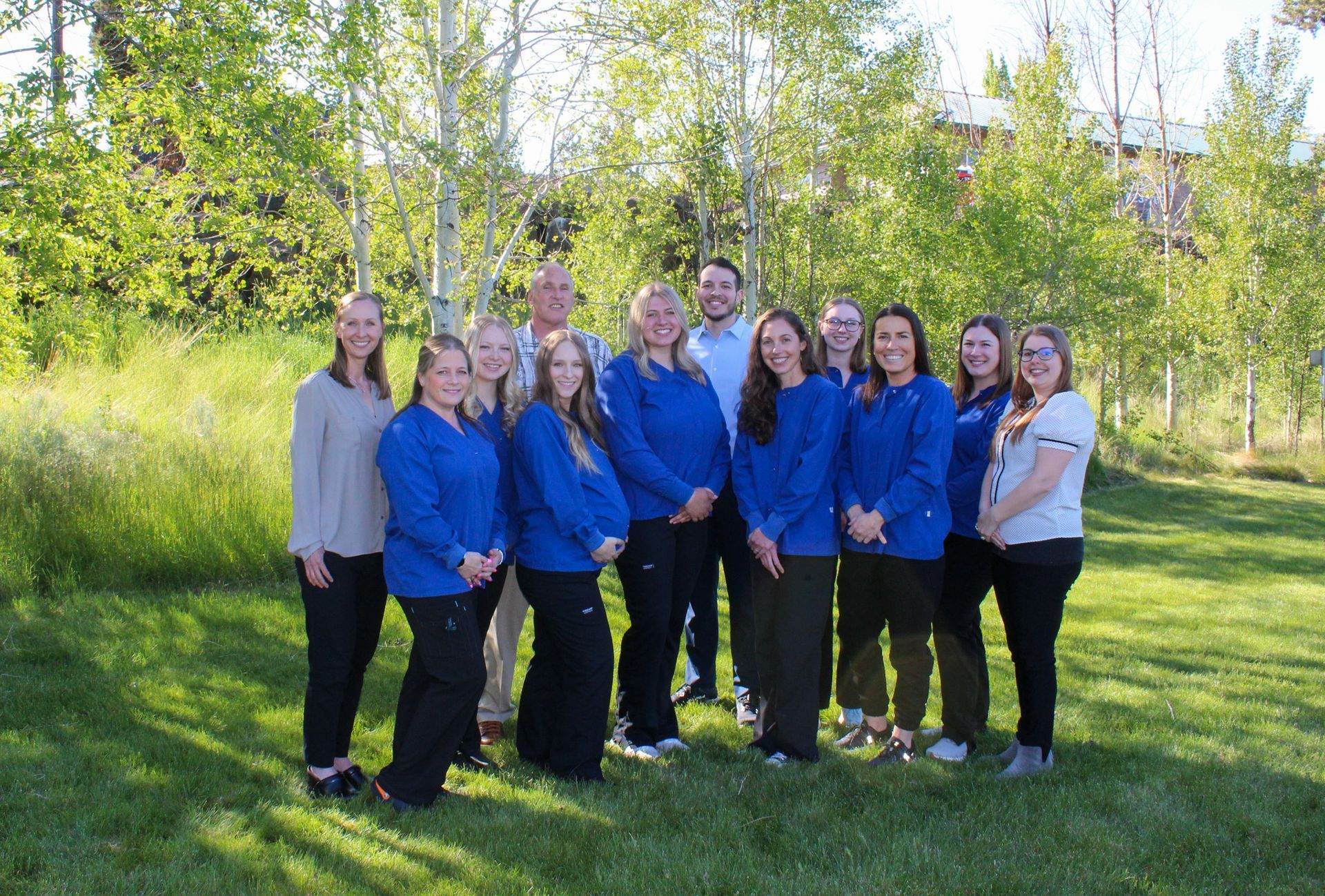 Group of people in blue shirts posing outside on a sunny day near trees.