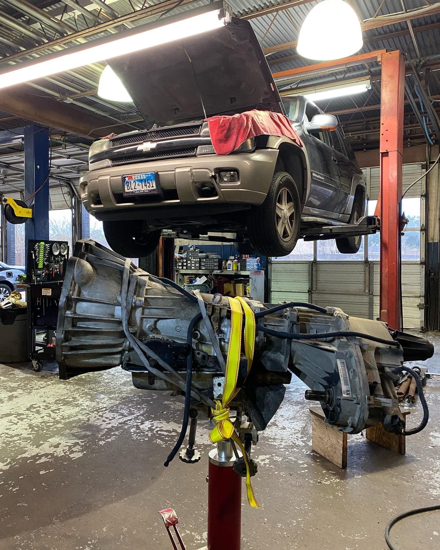 SUV on a lift in a garage, hood up.  A transmission is removed and sitting below. | Proline Auto