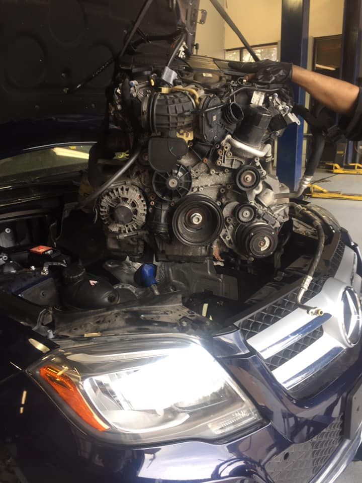 Car engine being lifted out of a dark blue Mercedes in a garage. Mechanic's arm visible. | Proline Auto
